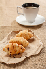 Fresh croissants on wrapping paper and cup of black coffee with saucer