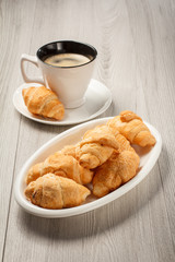 Cup of black coffee with saucer, fresh croissants on white porcelain dish