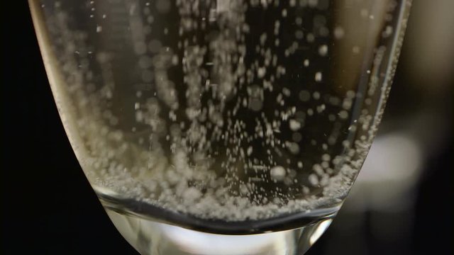 Bubbles of champagne rise from the bottom of the glass to the top. Black background. Close up