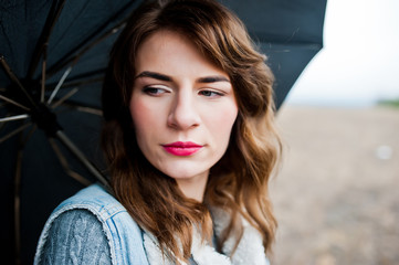 Portrait of brunette curly girl in jeans jacket with black umbrella at field.