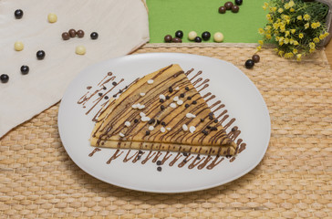 Folded crepe, Russian blini with chocolate sauce on white plate, chololate chips on topping and dragees on the table