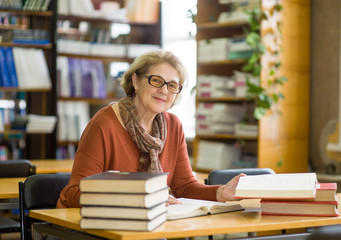 Happy senior woman with books in library looking at camera