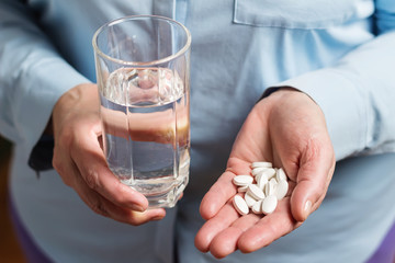 White medication pills, calcium dietary supplement in the woman palm hand and glass with water in the other hand - obrazy, fototapety, plakaty
