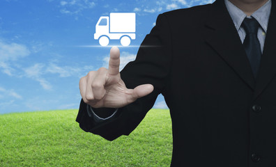 Businessman pressing truck delivery icon over green grass field with blue sky, Business transportation service concept