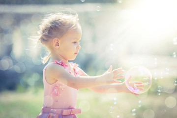 A little girl catches soap bubbles in summer park