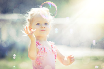 A little girl catches soap bubbles in summer park