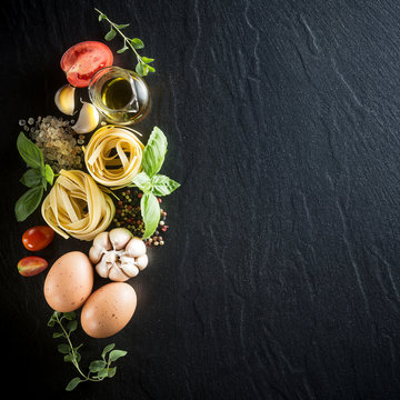 Italian food and ingredients background with fresh vegetables, eggs, tomatos, olive oil, oregano, garlic, salt, pepper, basil, pasta and spices. Top view, view from above. Copy space. Dark background.