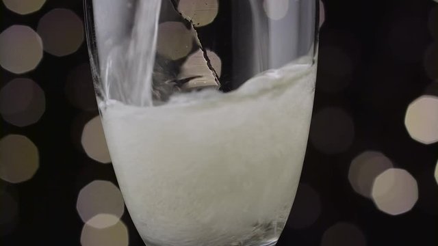 Champagne poured into a glass it foams to form a foam cap. Bokeh background. Close up