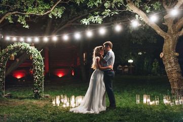 Enamored newlyweds gently embrace. Wedding ceremony in nature. The lights of the electric garland...