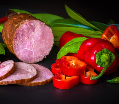 Smoked sausage, ham with red and green peppers and herbs on a dark background