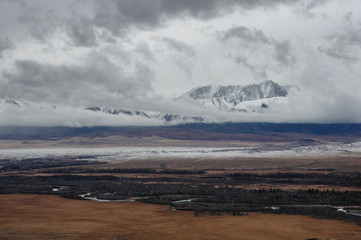 Dramatic winter dark desert steppe river on a highland mountain plateau with ranges of  snow peaks on a horizon storm skyline Kurai Altai Mountains Siberia Russia