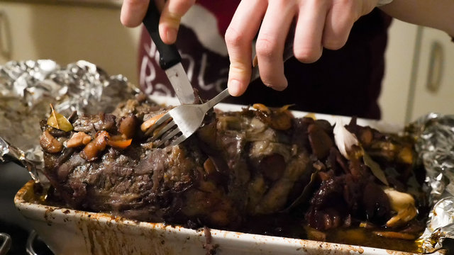 Female hands trying roasted beef cutting it by fork and knife on busy kitchen table