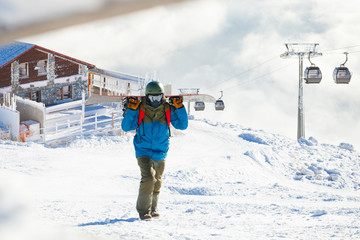 Winter sports concept - male snowboarder carrying his snowboard on shoulders at the top of a...