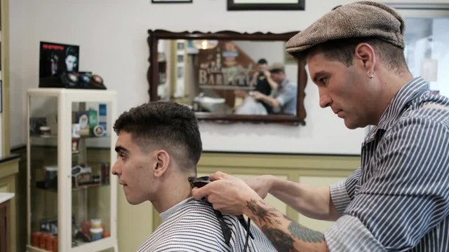 Hairdresser cutting young man hair in vintage male beauty salon