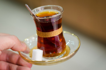Close-up of delicious red Turkish tea with traditional pear shaped glass with a teaspoon in the man...