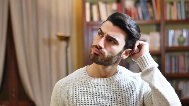 Confused or doubtful young man scratching his head and looking up. Indoors shot in a living room