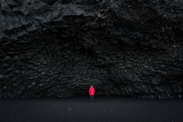 Woman in a red coat stands under Halsanefshellir Cave in Iceland