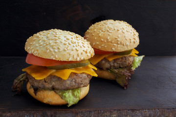 Tasty grilled delicious burger with lettuce, cheese, onion and tomato on a rustic wooden plank