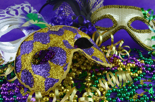 Mardi Gras image of close up detail of carnival masks, beads, ribbons and confetti in purple, green, gold and black on purple background