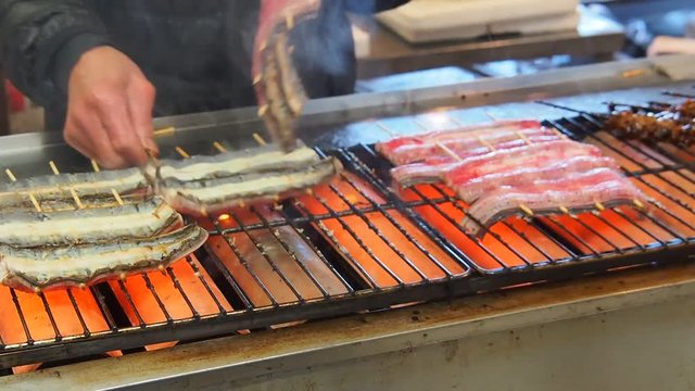 The chef is grilling skewered eels and livers on the stove