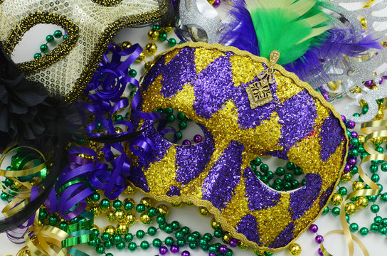 Mardi Gras image of close up detail of carnival masks, beads, ribbons and confetti in purple, green, gold and black on light background