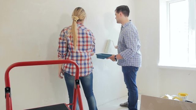 Slow motion footage of young man with wife painting walls with paint roller at new house