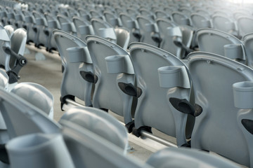 White plastic folding empty red seats in concert or football stadium. Row of football sport stadium seats with sunlight.