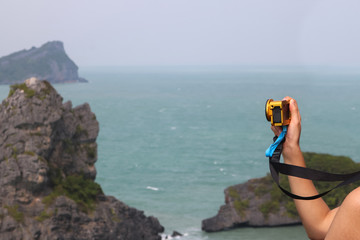 Hand with GoPro camera on top of mountain, Islands and ocean views background.