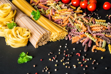 Various kind of italian raw Pasta. colorful fusilli pasta, spaghetti, fettuccine with tomatos on a black background. Closeup