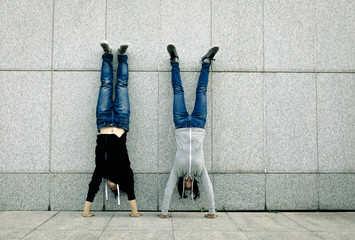 Two female hipster doing handstand against wall in city