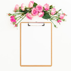 Spring composition with pink roses and clipboard on white background. Top view. Flat lay. Beauty blog, copy space