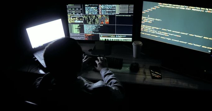 Young Hacker Breaks into Corporate Data Servers from His Underground Hideout. Place Has Dark Atmosphere, Multiple Displays