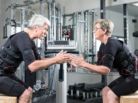 Pärchen im mittleren alter trainiert im Fitnessstudio mit einem EMS Gerät Stromimpulsgerät, Gummibänder, Kurzhanteln