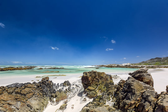 Beach view with white sand, rocks and crystal clear water at Brandfontein - Rietfontein Nature Reserve near Cape Agulhas, Western Cape Province, South Africa.