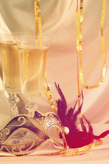 Image of elegant venetian mask and glasses of champagne over gold silk background.