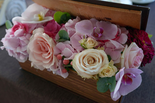 Rectangular wooden box containing a mixed pastel color flower arrangement with roses, orchids and berries suitable as a decor for table centerpieces at weddings or formal events