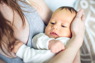 Happy caring mother holding a smiling baby boy in the bedroom. Concept of the tenderness of motherhood and family values