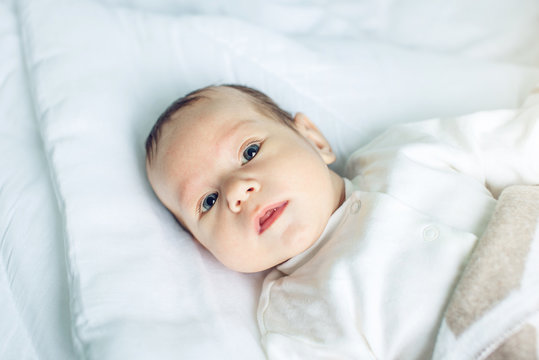 Cute funny baby lying on a white bed covered with a blanket. Concept of The tenderness of motherhood and family values