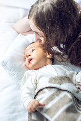 Happy caring mother holding a smiling baby boy and kisses him. Concept of the tenderness of motherhood and family values