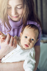 Happy caring mother holding a smiling baby boy in the bedroom. Concept of the tenderness of motherhood and family values