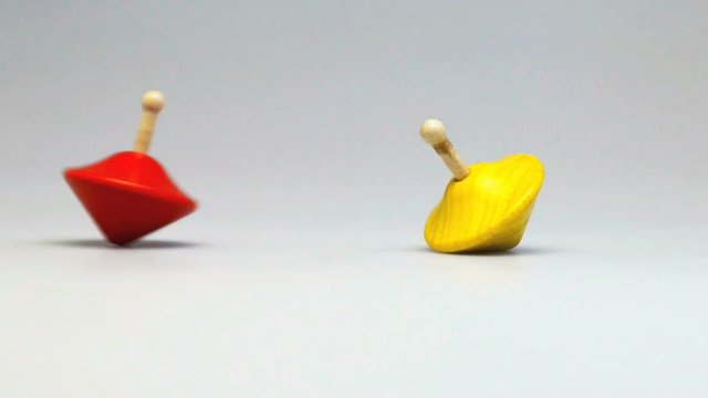 Cinemagraph - Two wooden and colorful spinning tops , red one in perpetual motion