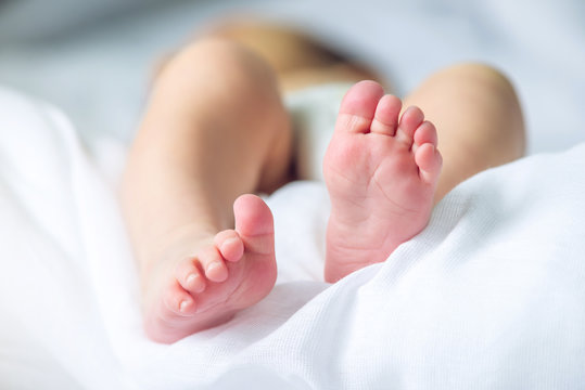 Baby feet with pink lying on a white blanket. Concept of tenderness and motherhood
