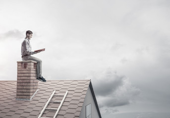 Handsome man on brick roof against cloud scape reading book
