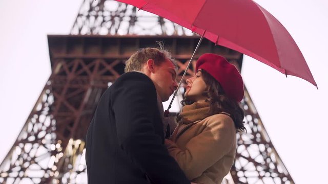 Beautiful young couple tenderly kissing under umbrella, romantic date in Paris