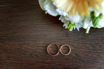 Beautiful wedding rings lie on a table against the background of a bouquet of flowers