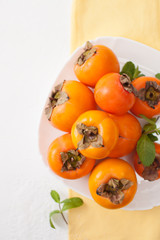 A bunch of ripe persimmons in a bowl on a white table