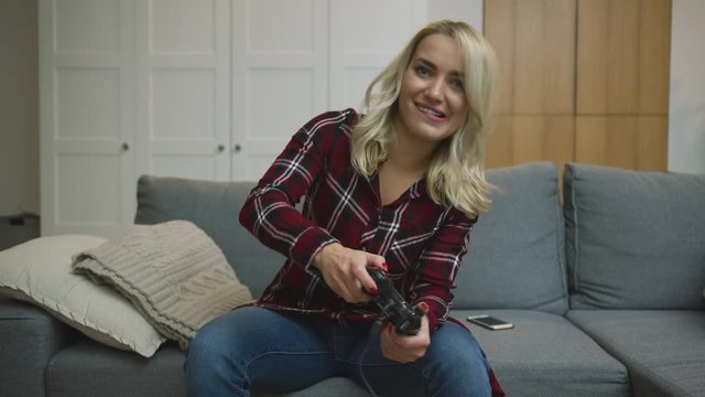 Lovely young woman in checkered shirt sitting on comfortable sofa and playing video games with excited face expression.