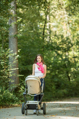 Fototapeta na wymiar Attractive stylish woman pushing a baby stroller along a rural road