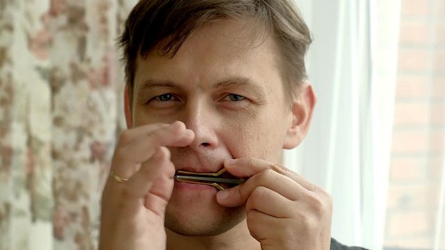 Portrait of a man playing a harp. The bearded shaman plays the harmonica drymba. Face close up with a musical instrument Jew's Harp.