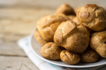 Homemade profiterole filled with cream without topping on a little white plate on the wooden table